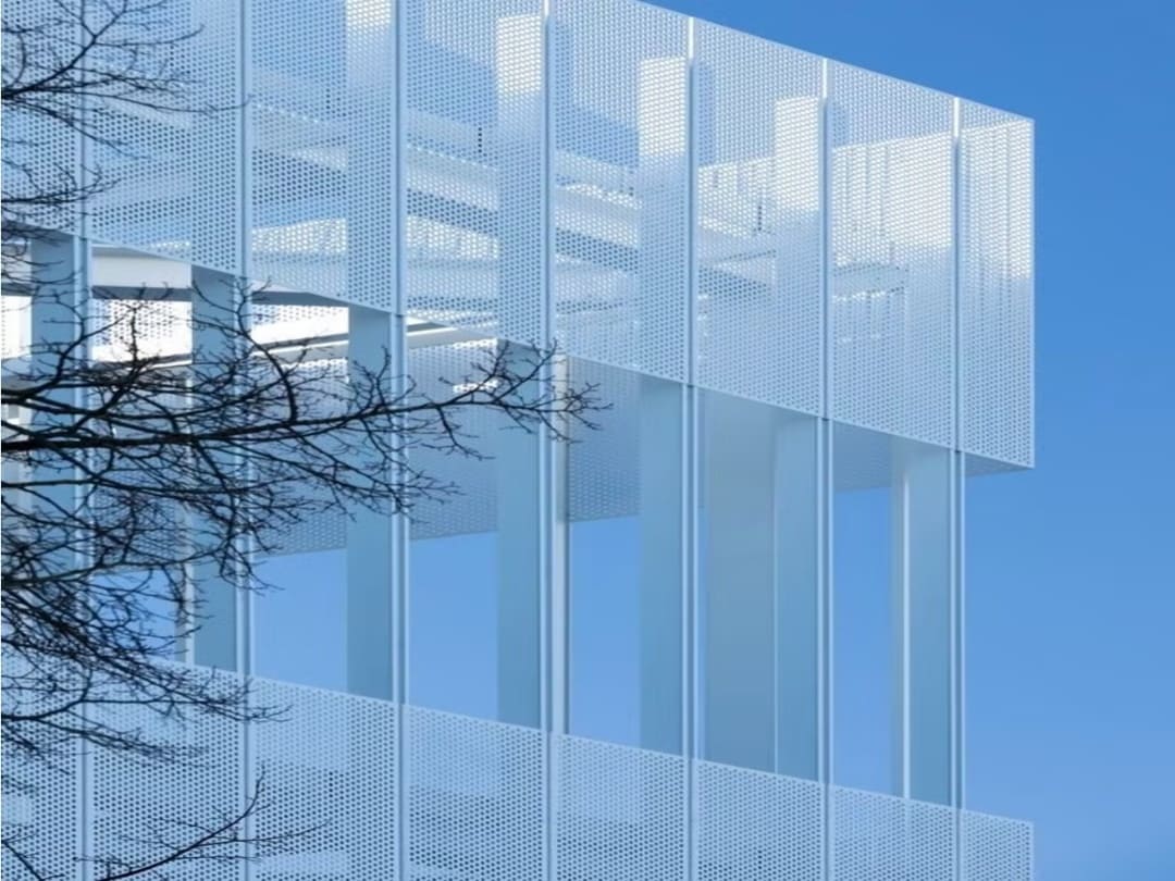 Modern architecture featuring a white perforated metal facade and vertical pillars against a clear blue sky