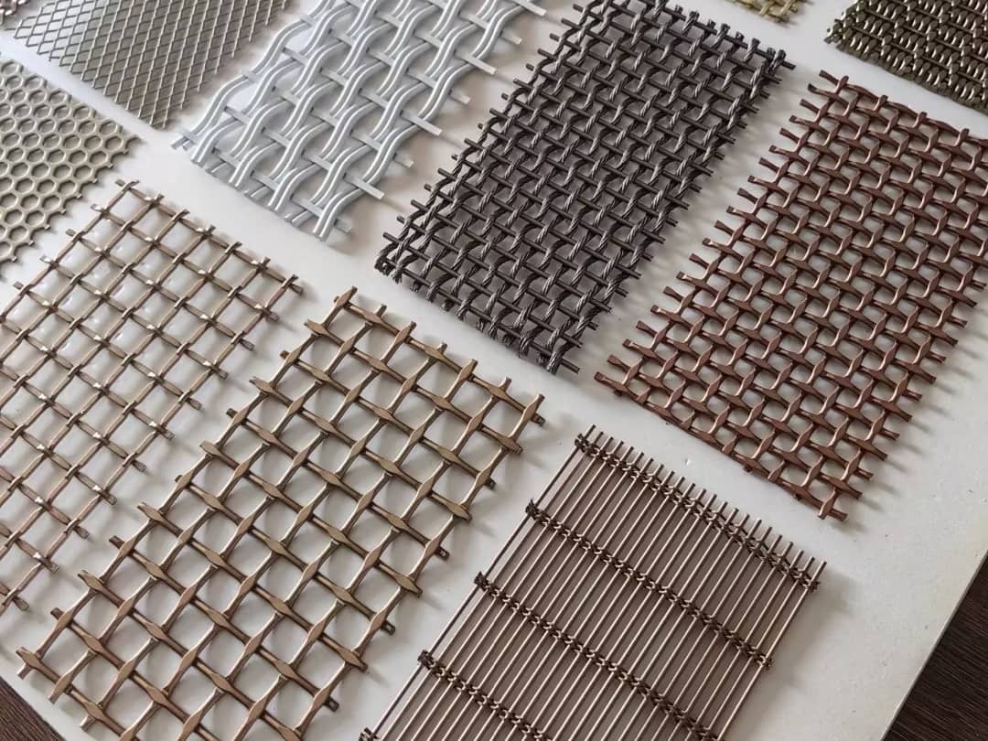 An array of architectural metal mesh samples in various weaves, colors, and materials, including woven wire, expanded metal, and cable mesh