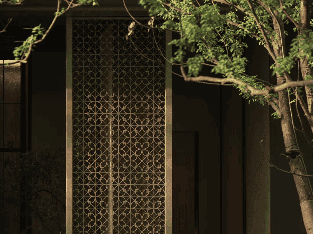 An elegant architectural detail featuring a decorative geometric screen panel nestled among lush green tree branches