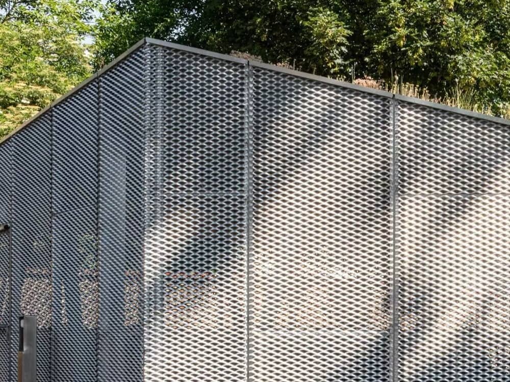 Modern building featuring a silver expanded metal mesh facade with a diamond pattern and sloped roof